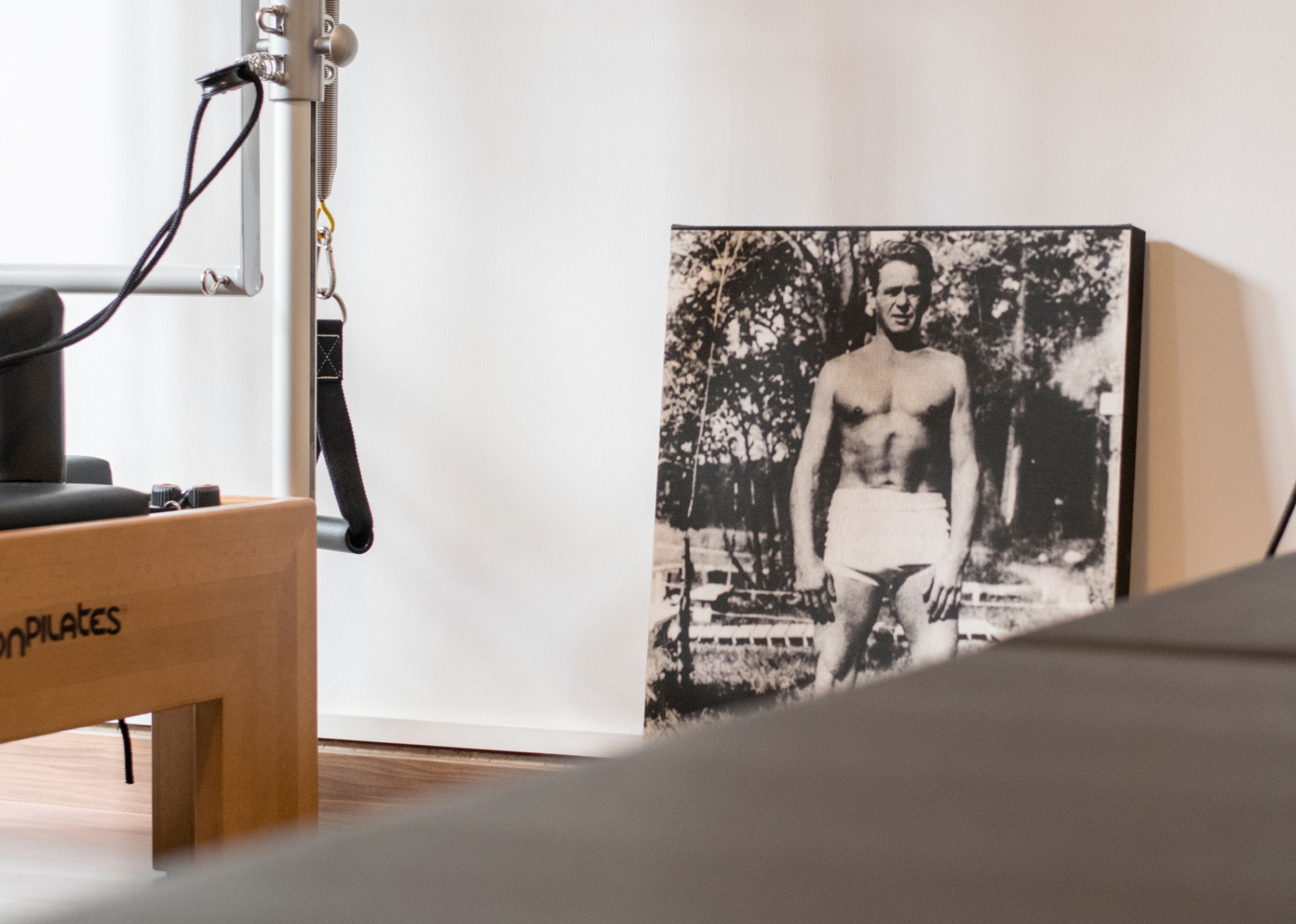 Retrato de Joseph Pilates junto a un reformer en el estudio SLOA